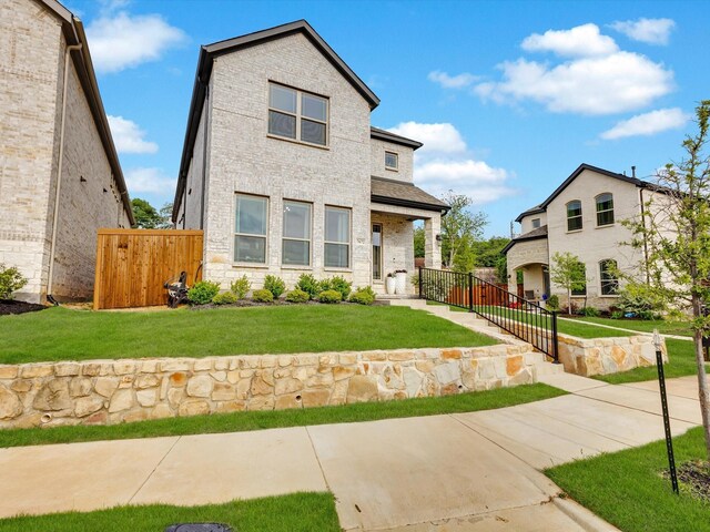 modern home featuring brick siding, a front lawn, and fence