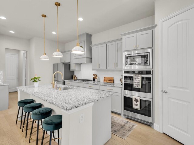 kitchen featuring a sink, a kitchen breakfast bar, stainless steel appliances, light wood-type flooring, and a center island with sink