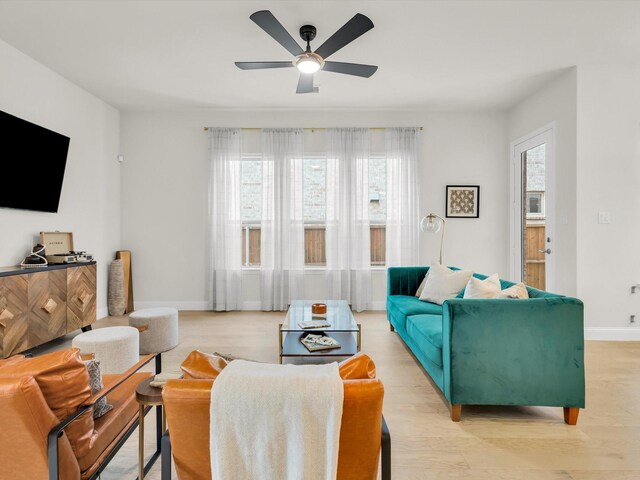 living room with baseboards, a ceiling fan, and light wood-style flooring