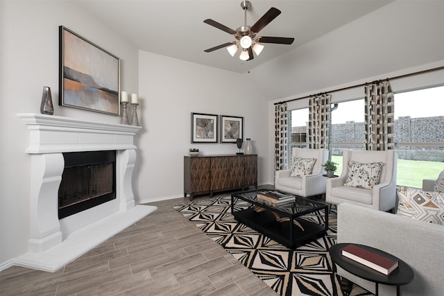living room featuring ceiling fan, wood finished floors, baseboards, a fireplace with raised hearth, and lofted ceiling