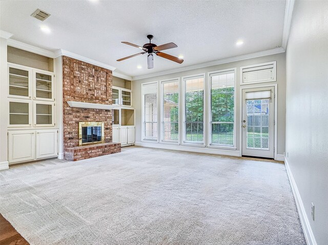 unfurnished living room featuring ceiling fan, visible vents, crown molding, a brick fireplace, and carpet floors
