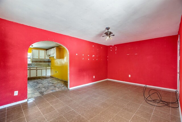unfurnished room with arched walkways, ceiling fan, and baseboards