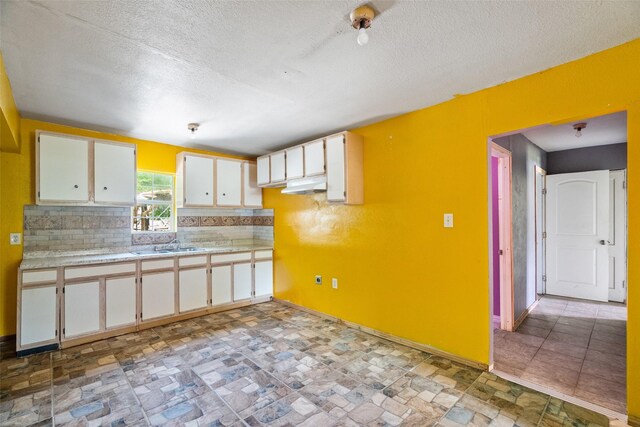 kitchen with white cabinets, light countertops, a textured ceiling, baseboards, and under cabinet range hood