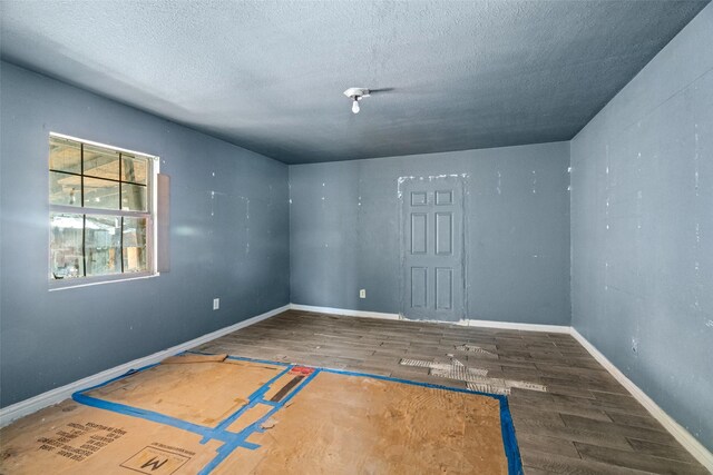 unfurnished room featuring a textured ceiling, baseboards, and wood finished floors