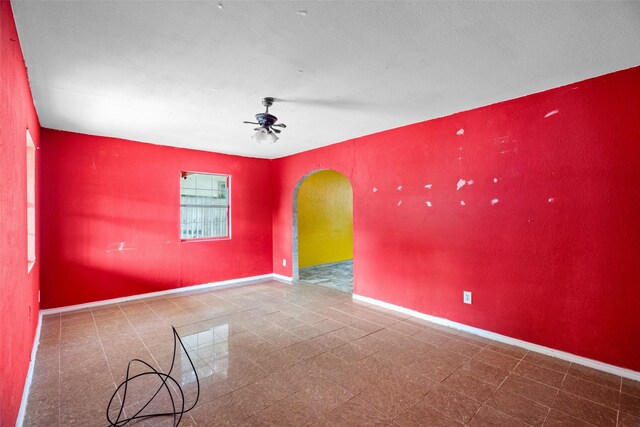 empty room with arched walkways, baseboards, and a ceiling fan