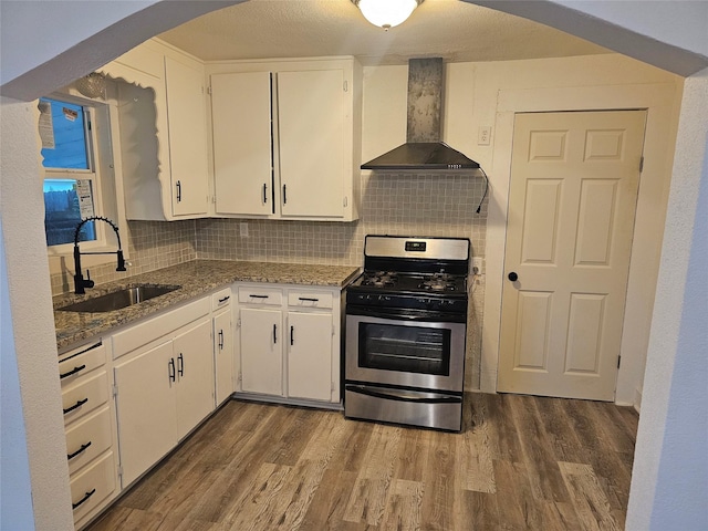 kitchen with dark wood-style floors, wall chimney exhaust hood, white cabinets, a sink, and gas stove