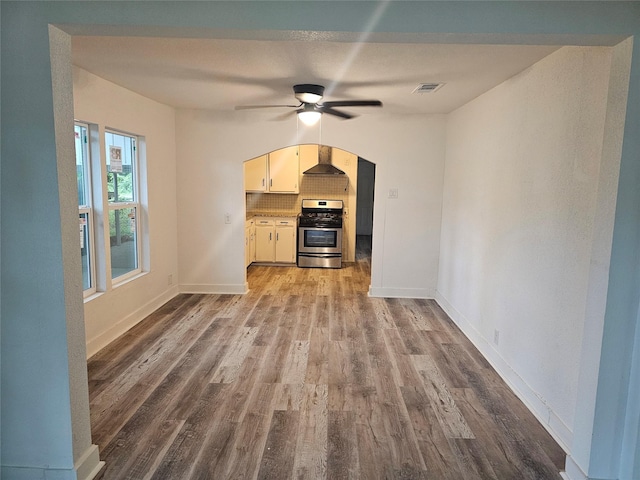 unfurnished living room featuring arched walkways, a ceiling fan, baseboards, wood finished floors, and visible vents