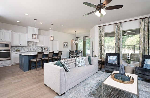 living area with recessed lighting, ceiling fan with notable chandelier, light wood-type flooring, and a wealth of natural light