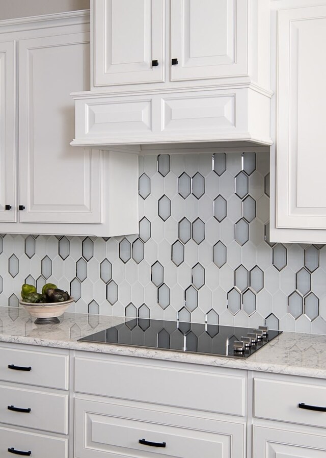 kitchen with light stone counters, white cabinets, backsplash, and black electric stovetop