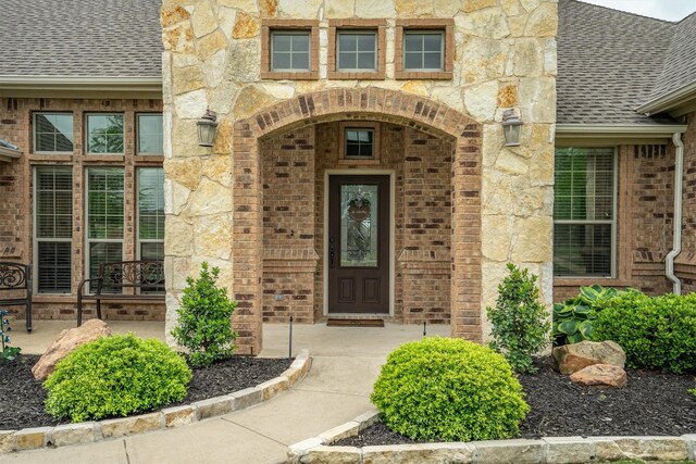 view of exterior entry with roof with shingles, stone siding, and brick siding