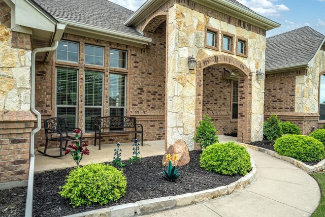doorway to property featuring brick siding, a shingled roof, and stone siding