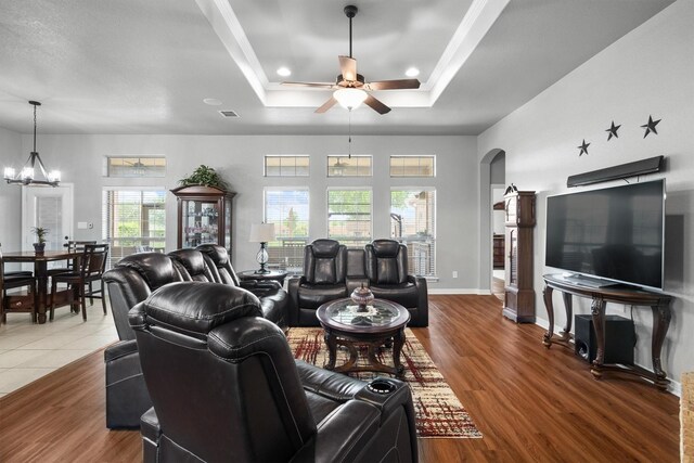 living room with visible vents, arched walkways, wood finished floors, a raised ceiling, and ceiling fan with notable chandelier