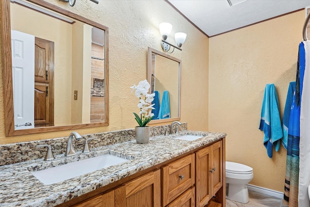 full bath featuring double vanity, toilet, a textured wall, and a sink