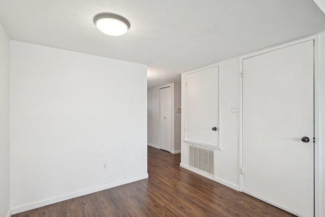 empty room with visible vents, dark wood-style flooring, and baseboards