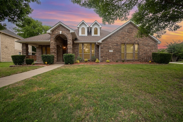 traditional home featuring roof with shingles, brick siding, and a front yard