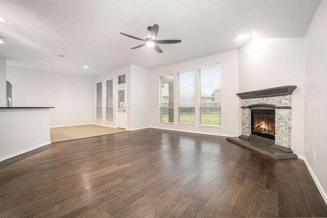 unfurnished living room featuring baseboards, ceiling fan, a fireplace, and wood finished floors