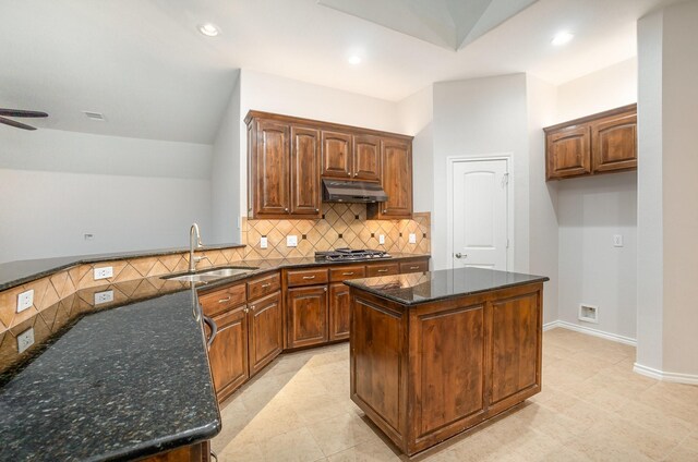 kitchen with a sink, dark stone counters, stainless steel gas stovetop, tasteful backsplash, and under cabinet range hood