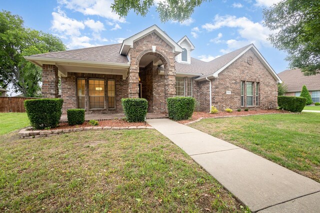 view of front of property featuring brick siding, roof with shingles, and a front yard