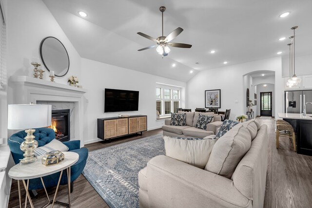 living room featuring ceiling fan, arched walkways, dark wood finished floors, lofted ceiling, and a premium fireplace
