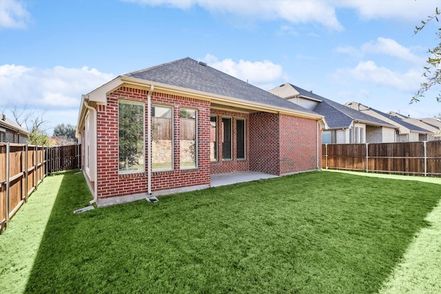 back of property with brick siding, a fenced backyard, roof with shingles, and a lawn