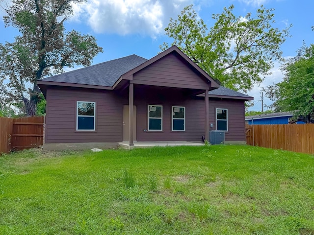 back of property with fence, central AC unit, a shingled roof, and a yard
