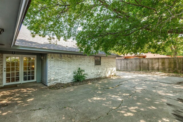 exterior space featuring brick siding, fence, a shingled roof, and a patio area