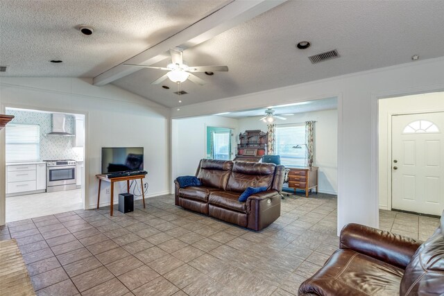 living area featuring ceiling fan, lofted ceiling with beams, a textured ceiling, baseboards, and visible vents
