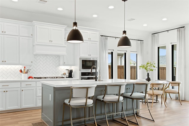 kitchen with tasteful backsplash, light countertops, white cabinetry, light wood-type flooring, and a center island with sink