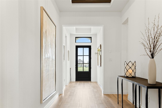doorway to outside featuring a raised ceiling, baseboards, and light wood finished floors