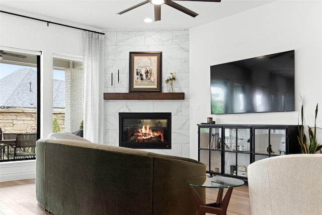living area with a tiled fireplace, a ceiling fan, and wood finished floors