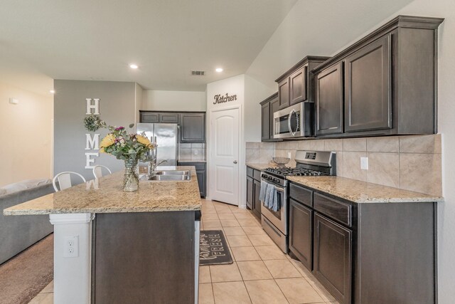 kitchen with light tile patterned floors, appliances with stainless steel finishes, a center island with sink, and a sink