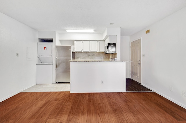 kitchen with backsplash, appliances with stainless steel finishes, stacked washer / dryer, and wood finished floors