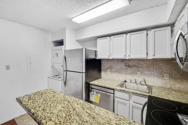 kitchen with decorative backsplash, stacked washer / dryer, a textured ceiling, a sink, and appliances with stainless steel finishes
