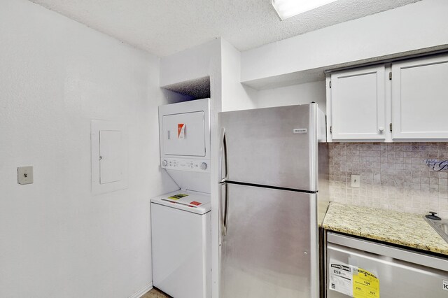 kitchen featuring white cabinets, stacked washer / drying machine, appliances with stainless steel finishes, light stone countertops, and decorative backsplash