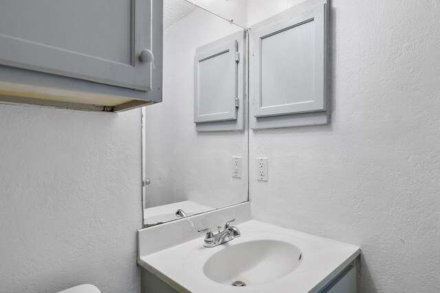 half bath with vanity and a textured wall