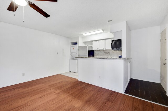 kitchen featuring freestanding refrigerator, stacked washer / drying machine, ceiling fan, light wood-type flooring, and backsplash