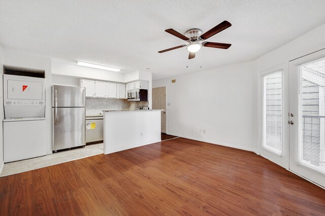 unfurnished living room featuring ceiling fan, stacked washer and clothes dryer, and wood finished floors