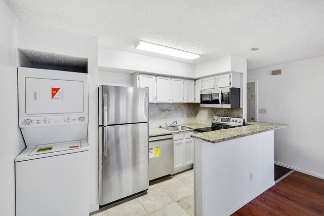 kitchen featuring backsplash, a textured ceiling, appliances with stainless steel finishes, stacked washing maching and dryer, and a sink