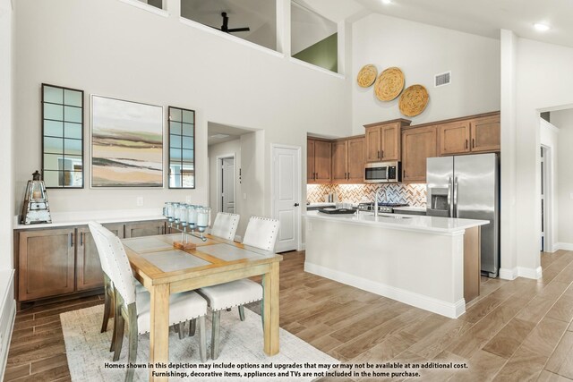 kitchen with brown cabinets, appliances with stainless steel finishes, high vaulted ceiling, light wood-style flooring, and visible vents