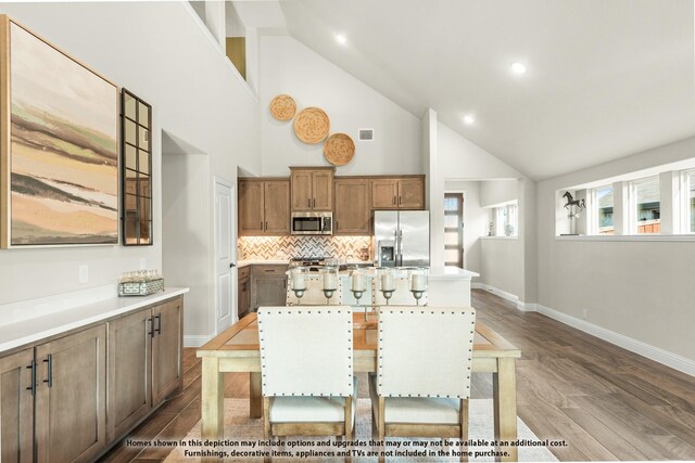 kitchen with brown cabinets, dark wood-style flooring, appliances with stainless steel finishes, tasteful backsplash, and a kitchen island