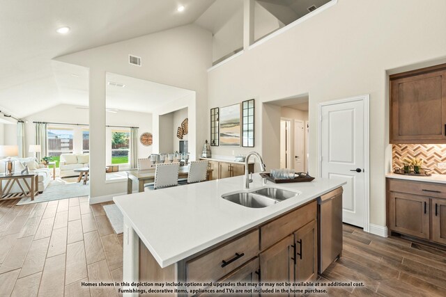 kitchen with visible vents, stainless steel dishwasher, open floor plan, a sink, and vaulted ceiling
