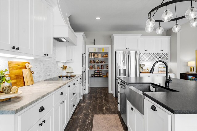 kitchen with custom exhaust hood, dark countertops, an island with sink, a sink, and stainless steel appliances