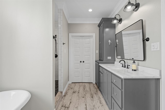 bathroom featuring crown molding, a tile shower, vanity, baseboards, and wood finished floors