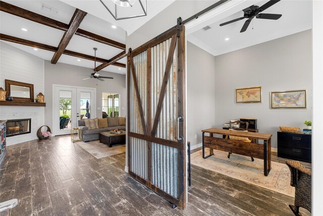 interior space featuring wood finished floors, a fireplace, beamed ceiling, a barn door, and a ceiling fan