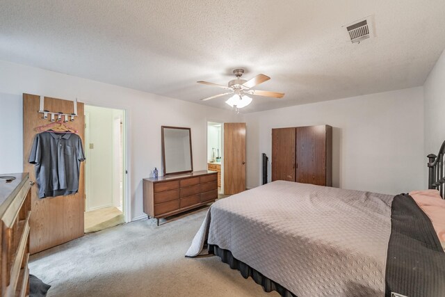 bedroom with light carpet, a textured ceiling, a ceiling fan, ensuite bathroom, and visible vents