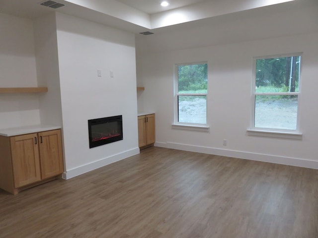 unfurnished living room with baseboards, a glass covered fireplace, light wood-style flooring, and visible vents