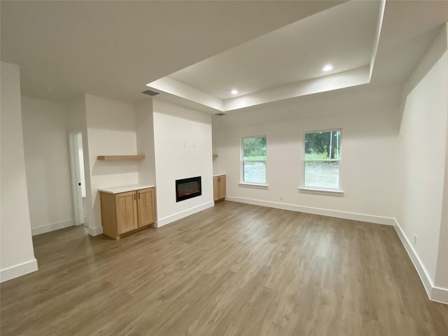 unfurnished living room with visible vents, light wood finished floors, baseboards, and a tray ceiling