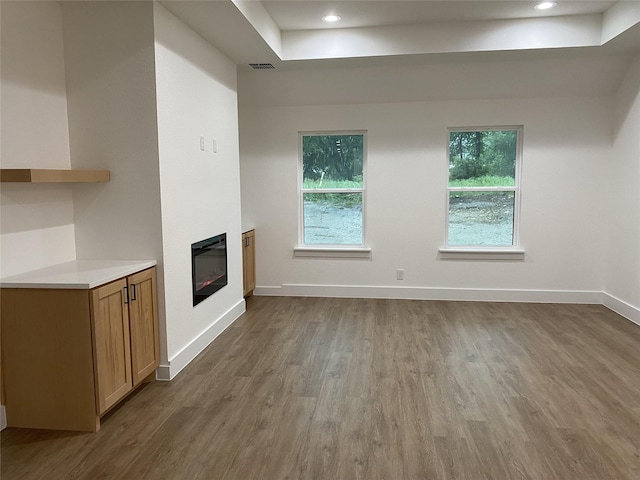 unfurnished living room with visible vents, a glass covered fireplace, wood finished floors, baseboards, and a raised ceiling