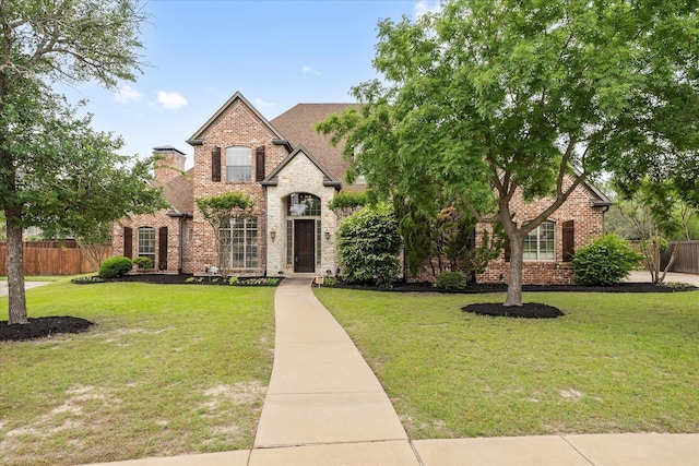 french country home featuring fence, a front lawn, and brick siding