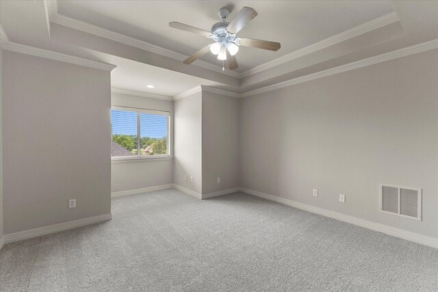 carpeted empty room featuring a ceiling fan, visible vents, baseboards, a raised ceiling, and ornamental molding